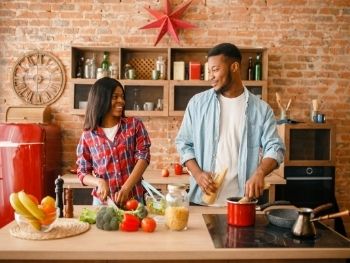 young-couple-cooking-in-brick-walled-kitchen-looking-at-each-other