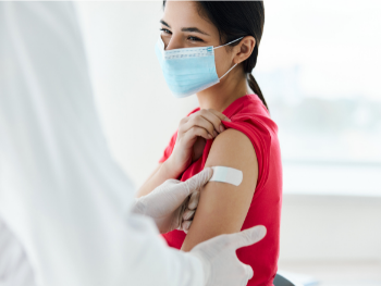 woman wearing a mask, smiling and getting a band-aid put on by a doctor