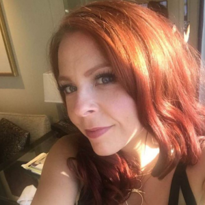 Woman with long red hair takes a selfie in a living room, with sunlight hitting the right side of her face