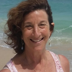 Woman with dark brown hair, standing on a beach.