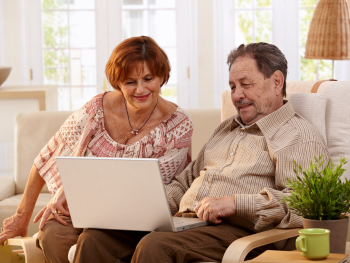 Older couple sitting on couch, looking at a computer together.